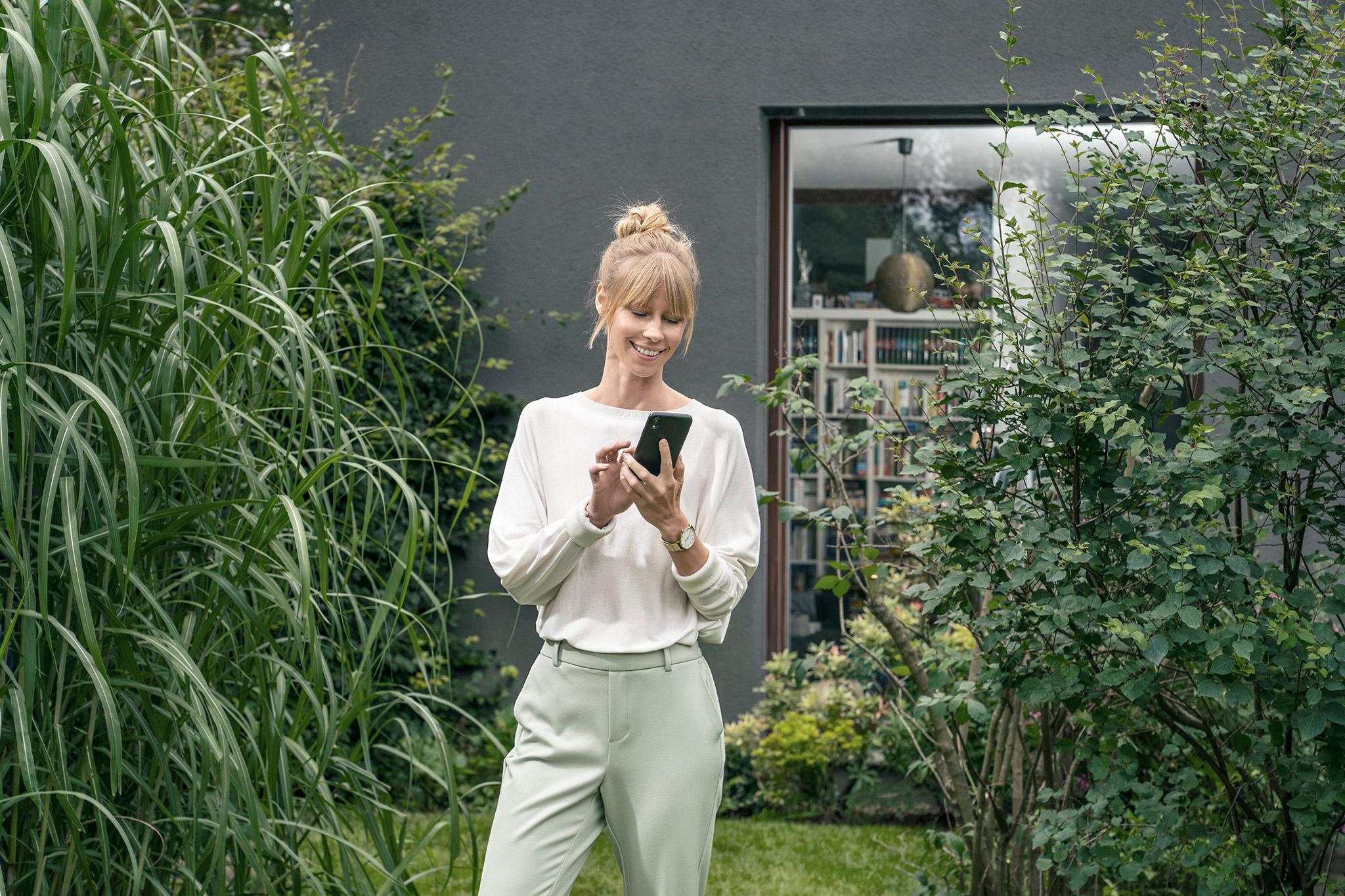 Kundin mit Handy im Garten – jetzt die KfW-Förderung sichern