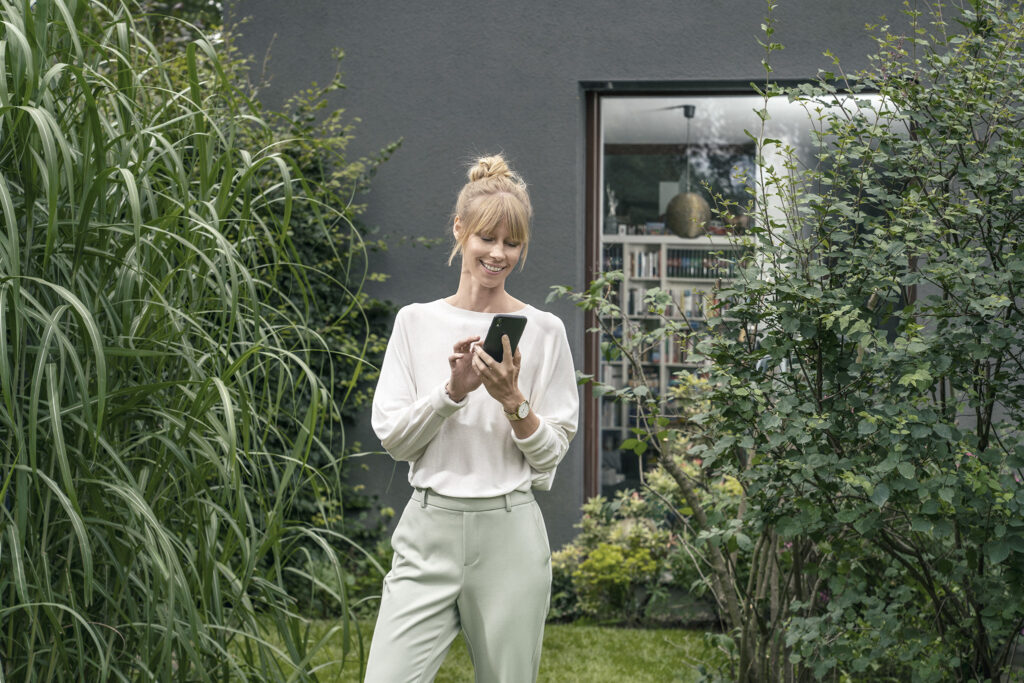 Kundin mit Handy im Garten – Photovoltaik als Kleinunternehmer mit zolar